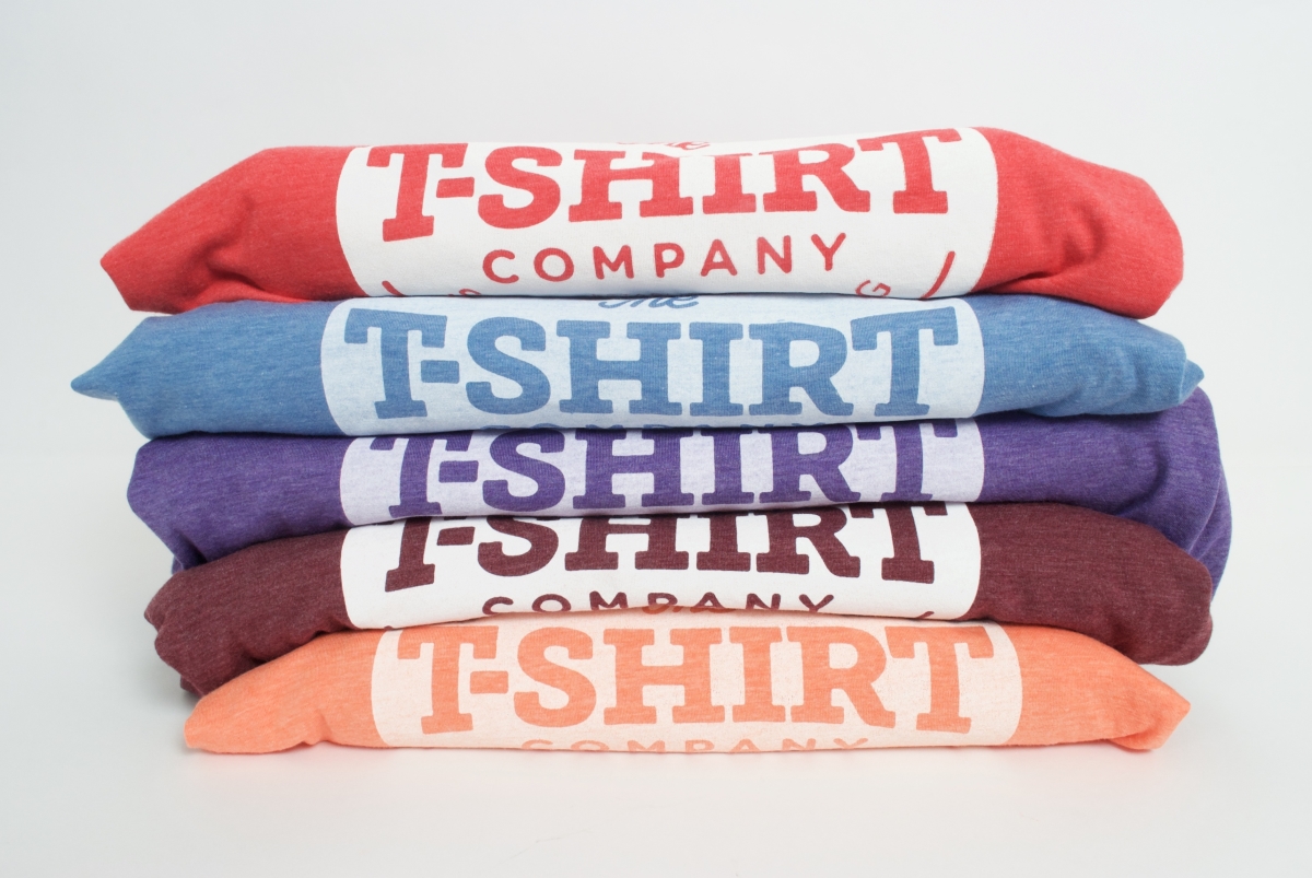 Five Bella and Canvas triblend tees in orange, red, blue,  purple and maroon stacked on top of each other with the t-shirt company logo clearly visible showing the different effects of white discharge ink on each colour way.